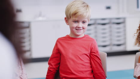 Young-white-schoolboy-sitting-in-class-listening-to-a-story-and-gesturing,-selective-focus