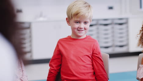 young white schoolboy sitting in class listening to a story and gesturing, selective focus