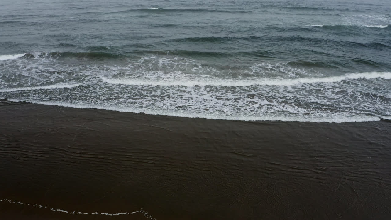 Vista dalla spiaggia di piccole onde dell'Oceano Pacifico che si infrangono a riva sulla costa dell'Oregon.