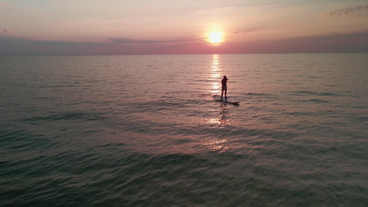 volo aereo via dell'uomo alzarsi in piedi paddle boarding nell'oceano al tramonto o al sorgere del sole
