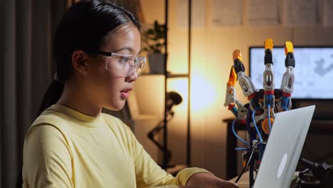 close up of teen asian girl working about a cyborg hand on a laptop at home