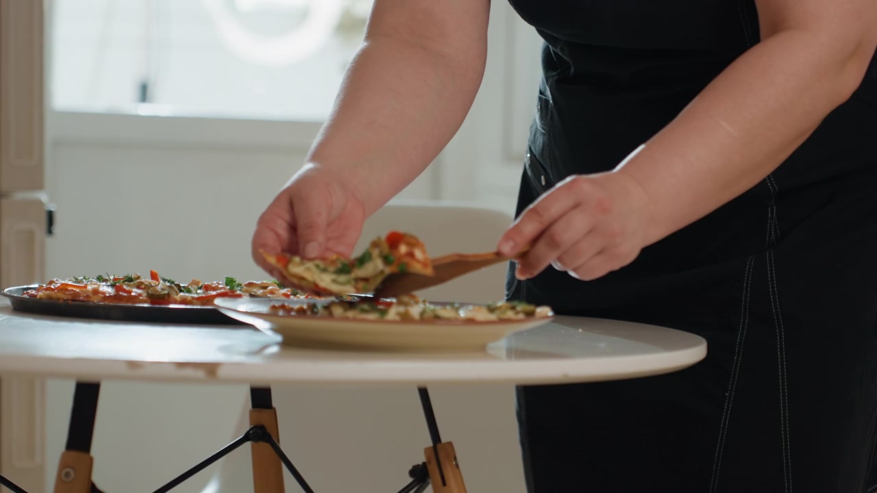 Close view of person using knife and spatula to cut, lift, and arrange sandwich on white round table in bright home kitchen, steadying pieces with other hand under warm window light