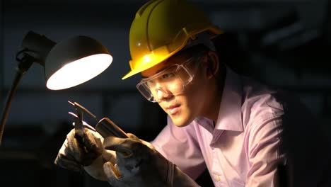 joven ingeniero asiático que trabaja y utiliza herramientas de medición de la calidad de las piezas metálicas. hombre que usa casco de seguridad con taller de trabajo. concepto de ingeniería, carrera, industria, fabricación, seguridad