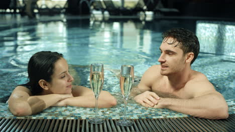 Attractive-couple-talking-in-jacuzzi-inside.-Sweet-guy-and-girl-chilling-in-spa