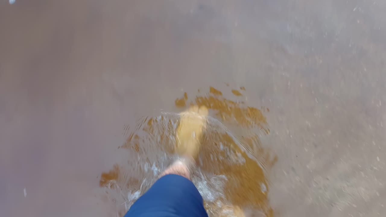 Barefoot man's feet walking on sand with crystal clear water. Close up