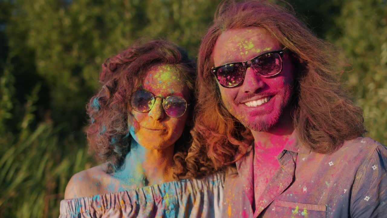 Mixed race couple with colorful faces and hair smiling during Holi festival having fun outdoors