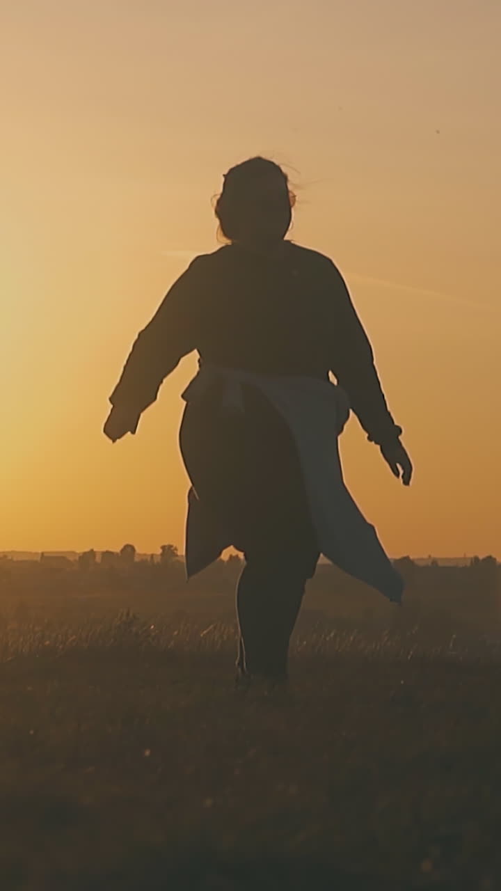 joyful plump girl silhouette dances near friends resting in tourist camp in autumn evening at back sunset slow motion