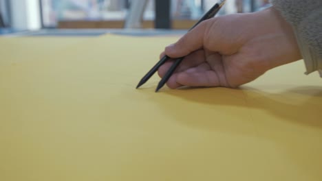 artista dibujando con dos lápices sobre papel amarillo