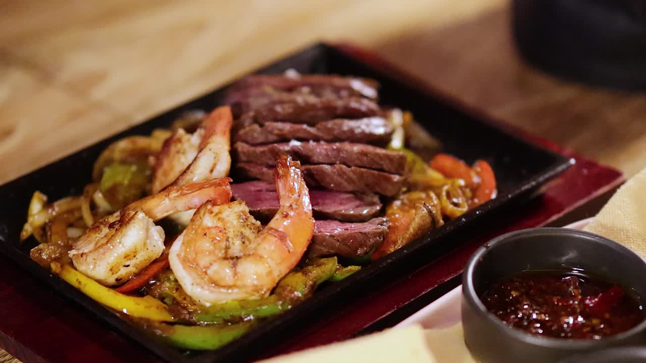 A close-up of sizzling beef and shrimp fajitas with sauces on a wooden table, transitioning to a focus on napkins
