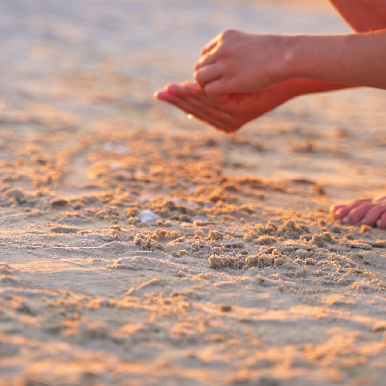 Close-up boys hands playing in sand at sunset. Boy putting different pebbles into sand in the evening. Child is having fun during summer holidays.