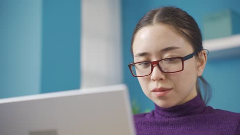 asian woman with glasses reading from laptop with focus.