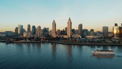 Downtown-San-Diego-Skyline-Over-The-Water-Aerial-at-Sunset-and-Tourist-Boat