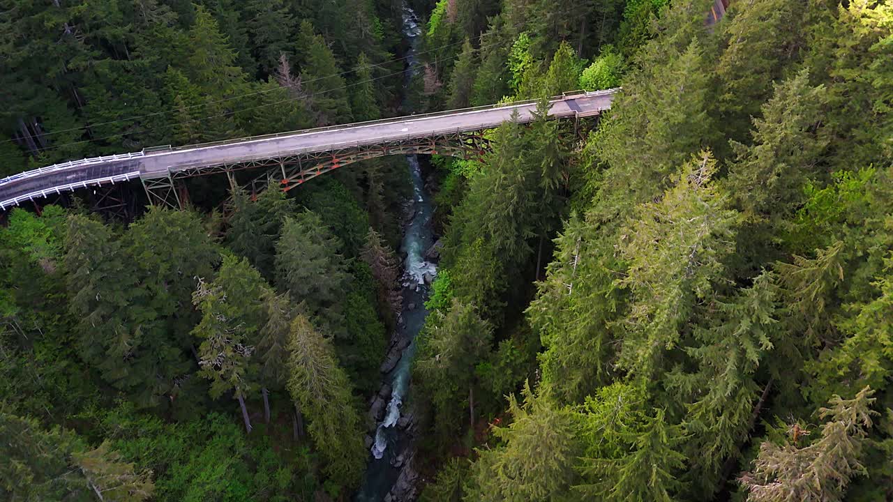 fotografía aérea panorámica volando sobre un río que fluye y un bosque de hoja perenne con un puente de acero en carbonado, estado de washington