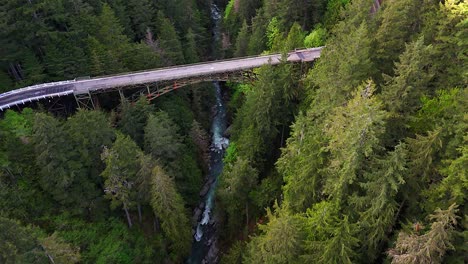 Toma-Aérea-Panorámica-Sobrevolando-Un-Río-Y-Un-Bosque-Siempre-Verde-Con-Un-Puente-De-Acero-En-Carbonado,-Estado-De-Washington.