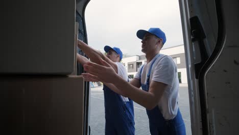 two young workers of removal company are loading boxes and furniture into a minibus