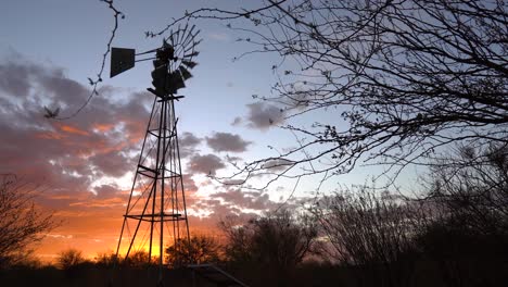 una bomba de viento contra una dramática puesta de sol con nubes naranjas en una granja de ovejas cerca de keetmanshoop, namibia