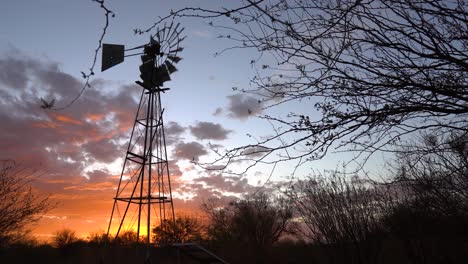 windpump against a dramatic sunset with orange clouds on a sheep farm near keetmanshoop, namibia