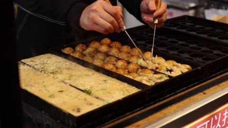 hands flipping takoyaki on a specialized grill