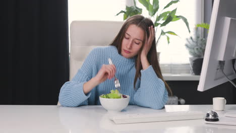 mujer infeliz sentada en el escritorio y comiendo ensalada saludable 1