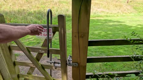 a person in a blue sleeve opens a wooden gate with a 'close the gate' sign, revealing a grassy garden path in daylight. camera remains steady