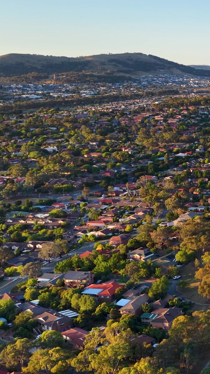 Una ripresa aerea con drone cattura un quartiere residenziale a Canberra durante una calda illuminazione al tramonto.