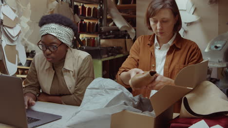 women packing shoes in box and using laptop in shoemakers workshop