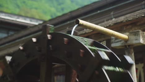 close up of water coming out of pipe onto spinning traditional water wheel in village town of shirakawago