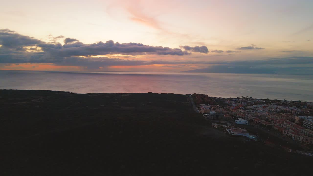 antena de carro hacia atrás de puesta de sol naranja y azul con vistas a un pequeño pueblo en la ladera de la montaña y al mar