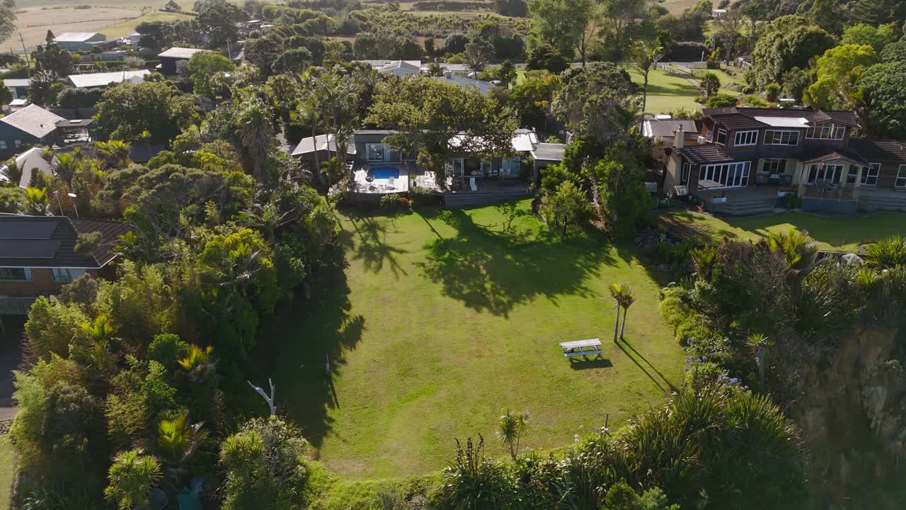 Luxury villas and mansion with large garden and Swimming pool at golden sunset in Muriwai beach, New Zealand. Aerial view.