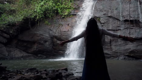 happy woman raised her arm while standing in front of waterfall, people enjoying vacation