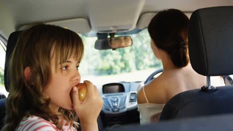 girl having apple in the back seat of the car