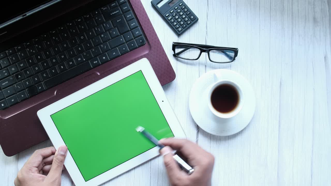Person using tablet with green screen, working on laptop