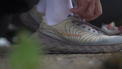 a person is putting on and tying the laces of a gray hiking and trail running shoe, wearing white socks