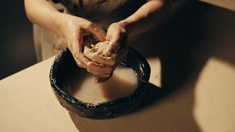 hands kneading clay in a bowl