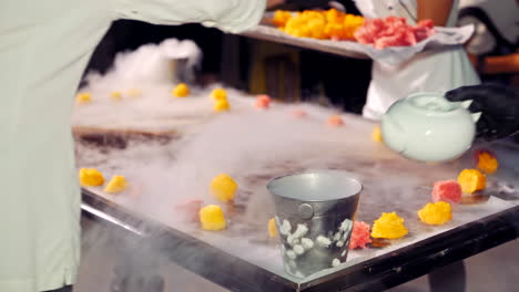 Chef and his assistant are putting fruit on the ice-cream background with steam. Preparation of delicious cold ice-cream with liquid nitrogen.