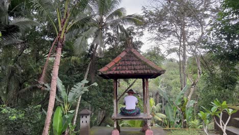 Tranquil-Balinese-Serenity:-Young-Male-Tourist-in-Anjali-Mudra-Pose-at-Goa-Gajah-Temple-Gazebo,-Bali-Rainforest-View