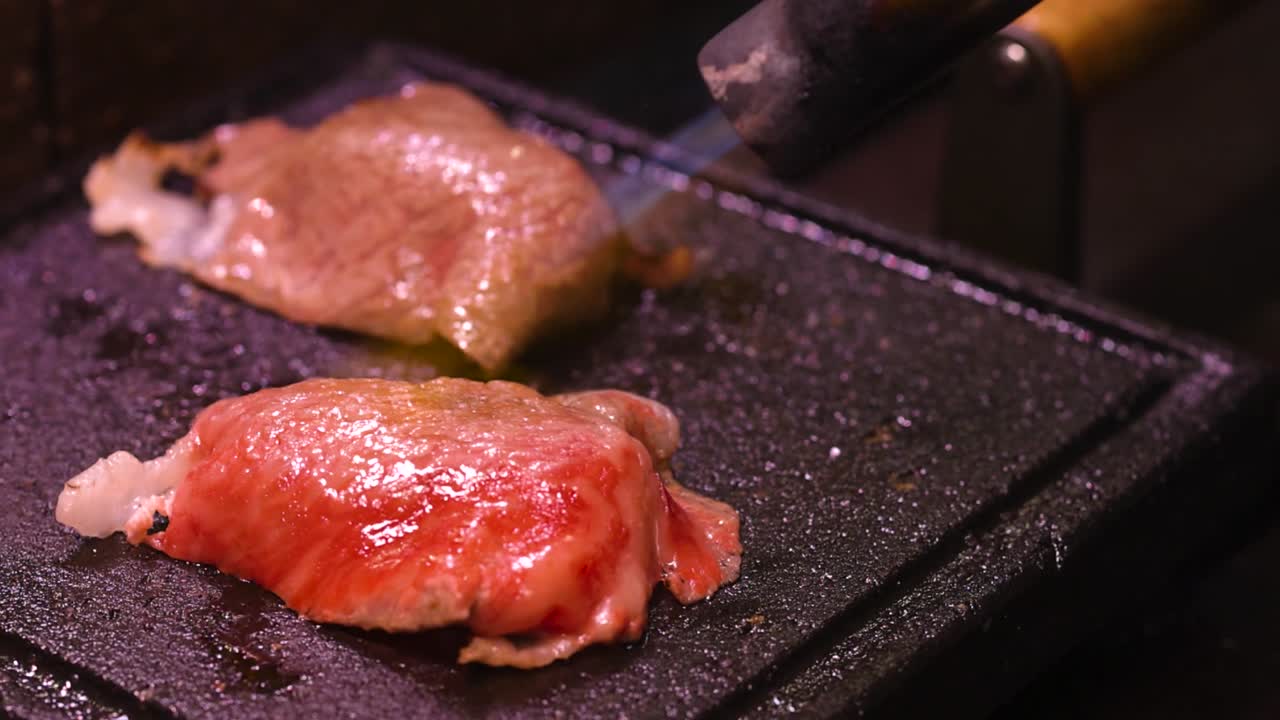 Detailed view of steak pieces being seared with a blowtorch on a grill surface.