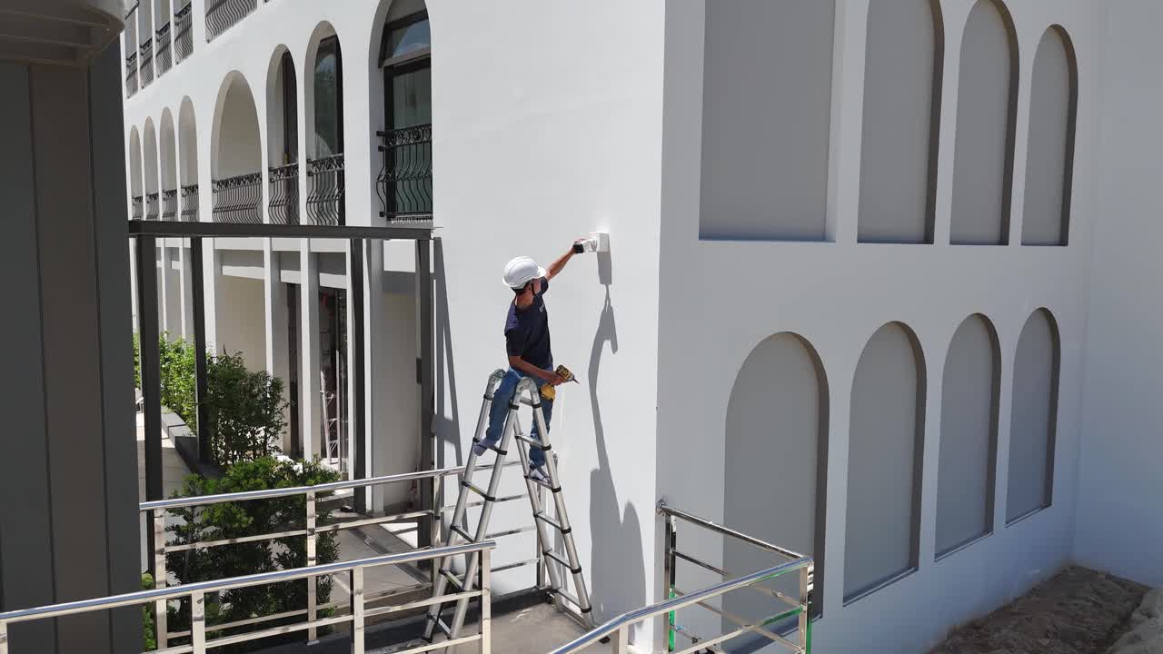 Worker installing a device on a white building exterior