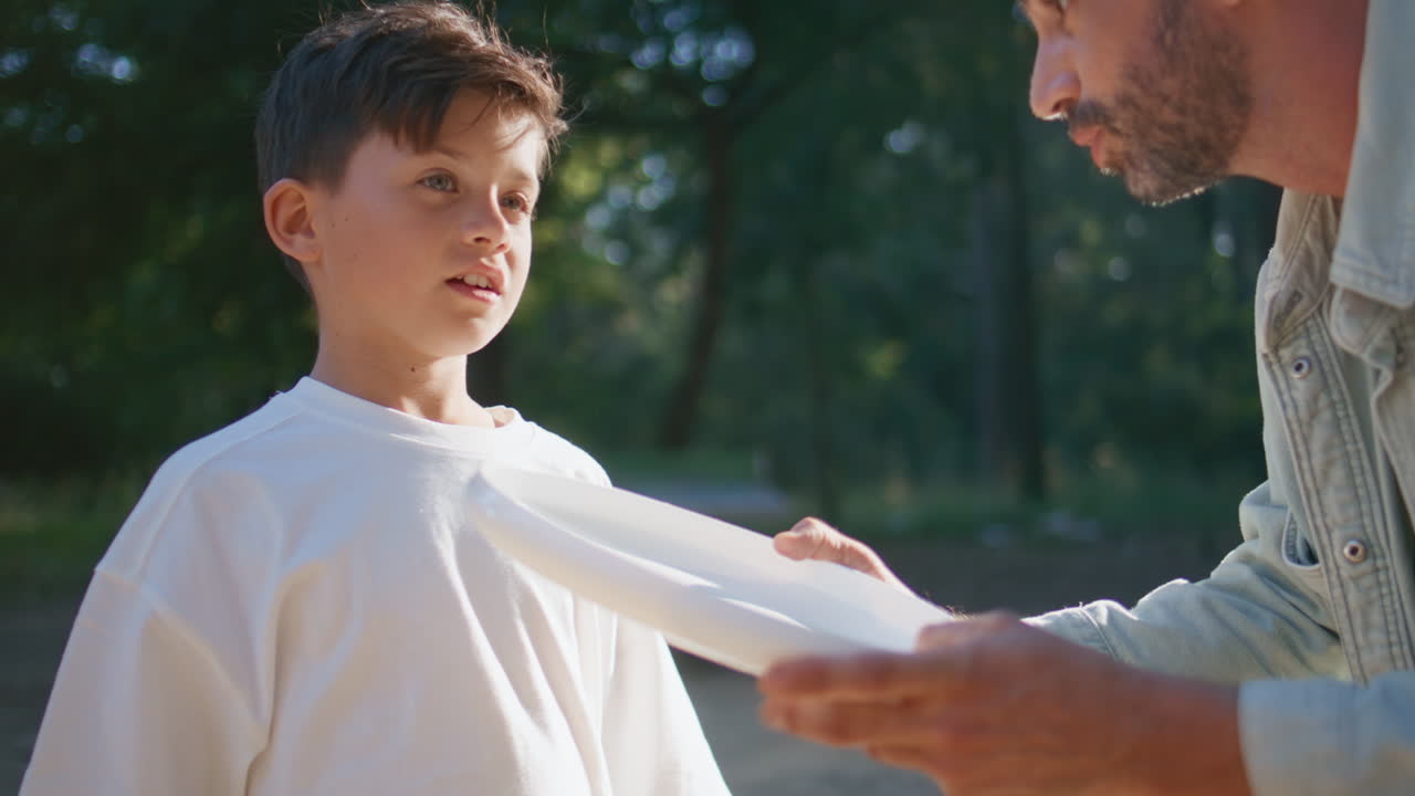 Father showing frisbee game technique to small child at sunny forest closeup