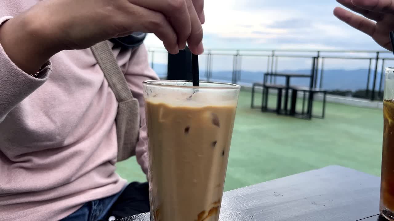 Donna che mescola un bicchiere di caffè latte freddo in una caffetteria panoramica.