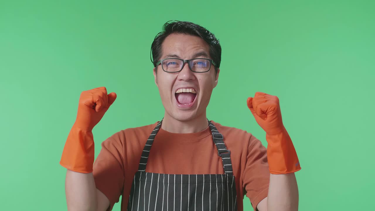 초록색 스크린 스튜디오에 서서 축하하는 아프론을 입은 행복한 아시아 남성 집주인의 클로즈업
