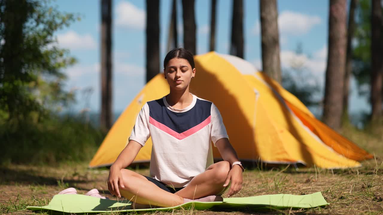 una adolescente meditando en un bosque cerca de una tienda