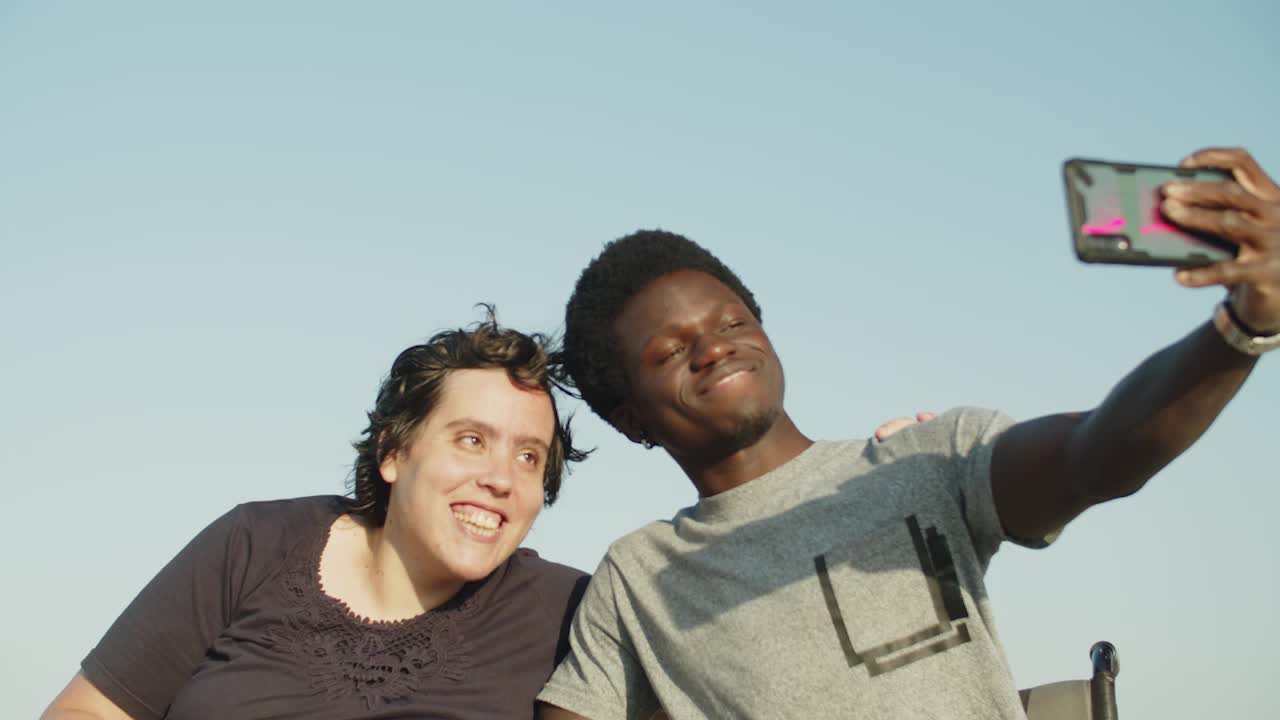 pareja alegre usando sillas de ruedas tomando selfies con teléfonos inteligentes