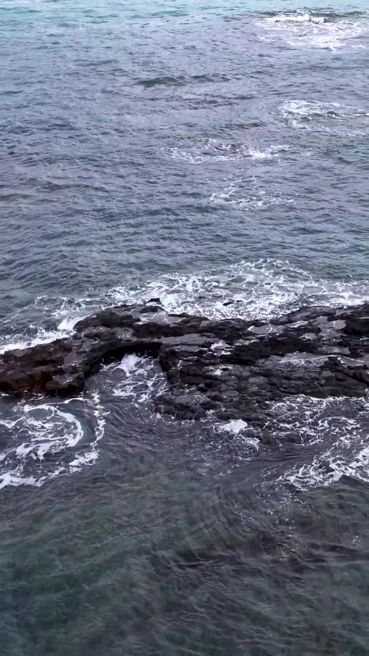 Vista dall'alto di acqua di mare turchese che si avvolge intorno a scogli vulcanici scuri della barriera corallina in Australia