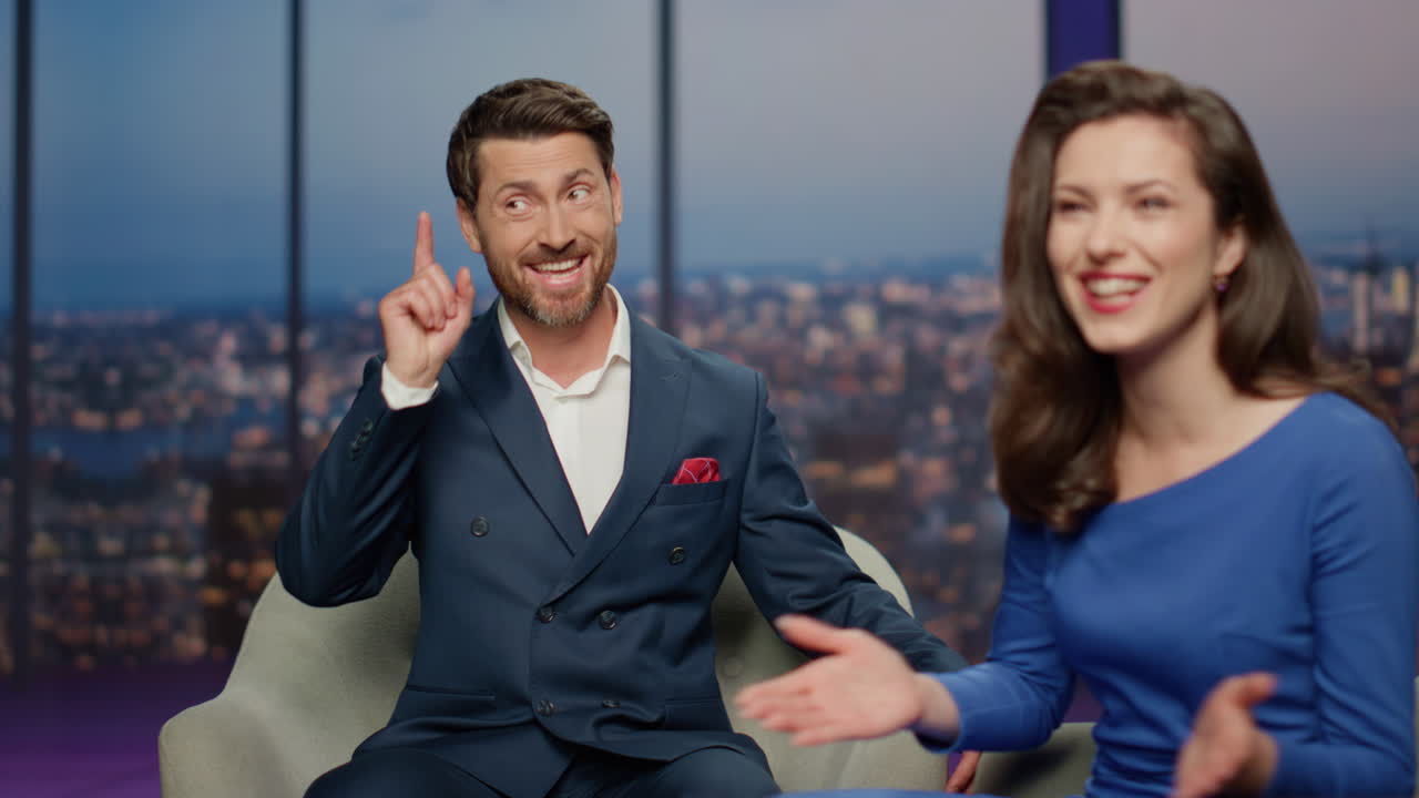 el presentador de un programa de entrevistas hablando con una mujer sentada en el estudio de un canal de televisión de cerca.