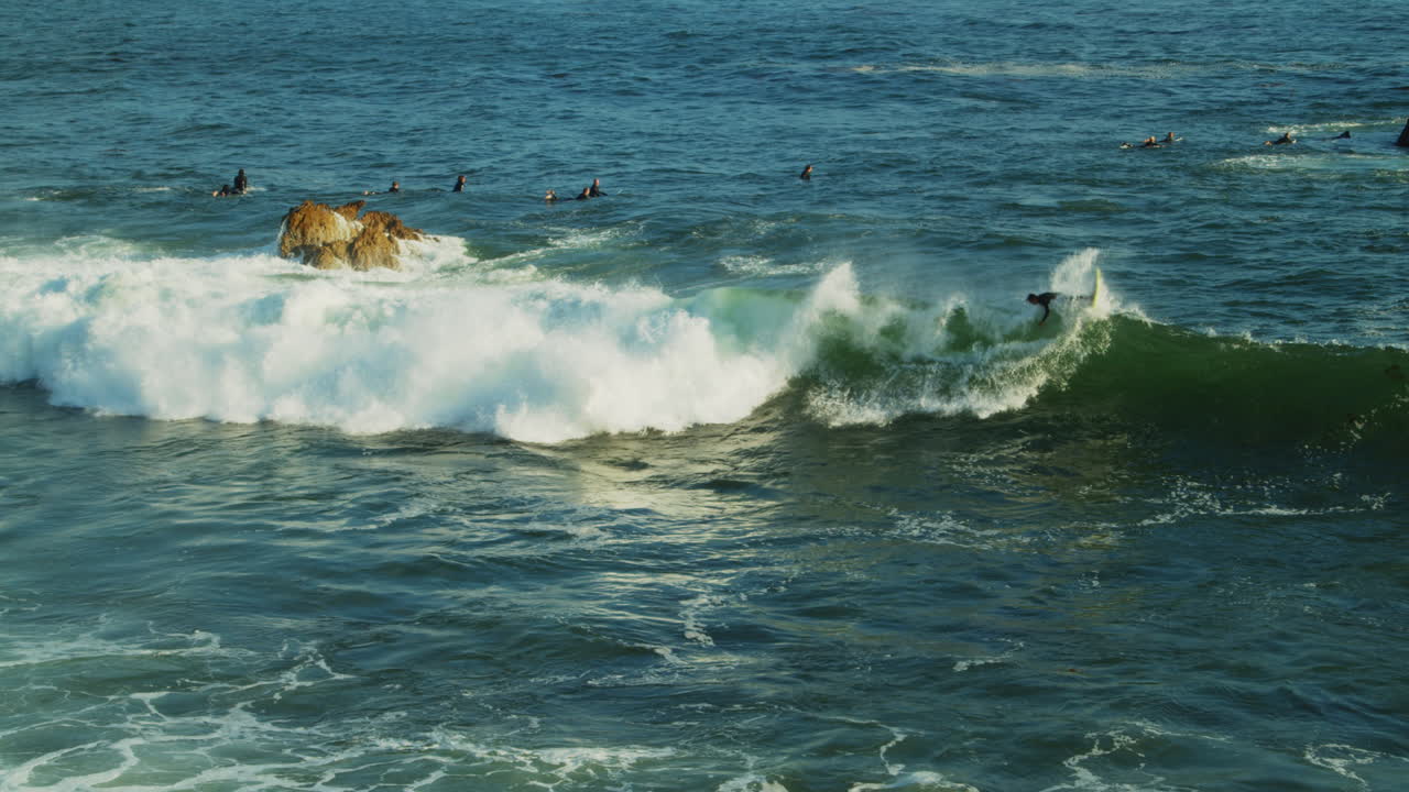 un surfista atrapando y montando una ola mientras otros en el agua miran frente a la costa del sur de california