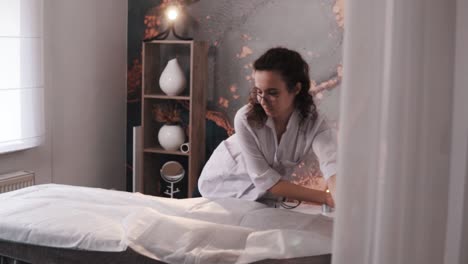 un cosmetólogo o masajista prepara su espacio de trabajo cubriendo la cama con una nueva sábana desechable para los próximos clientes en un salón de belleza con un interior elegante