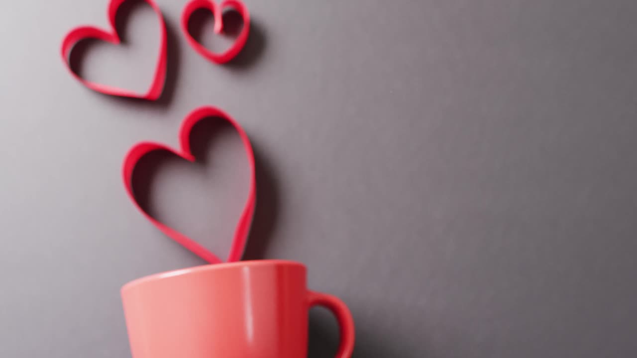 video de taza roja y formas de corazón rojas flotantes, en fondo gris con espacio de copia