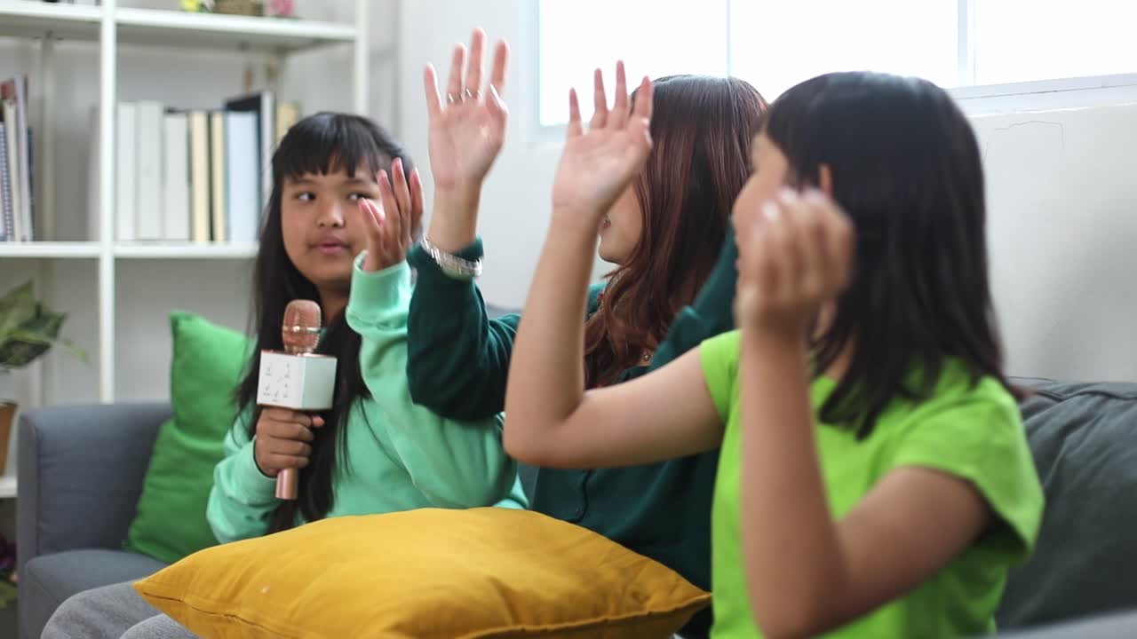 Happy Asian Family Mother And Child Daughters Play At Home, Waving Hand And Singing Together