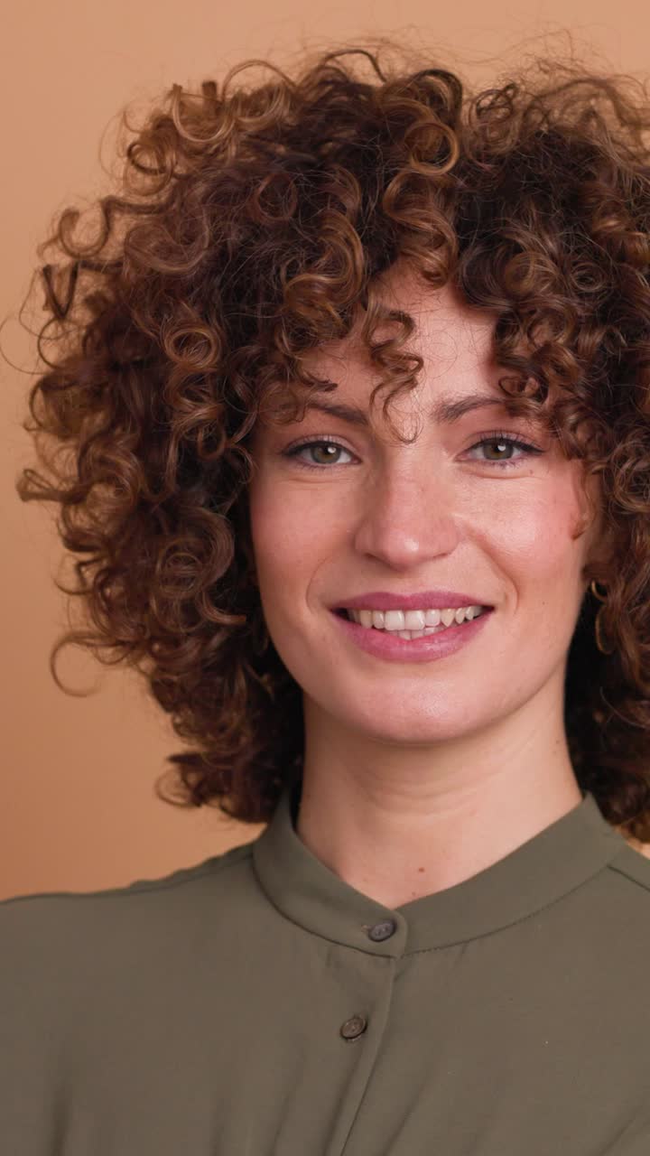 Smiling standing young curly haired woman on beige background. Vertical orientation